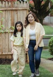 A woman and a little girl are walking down a sidewalk holding hands.