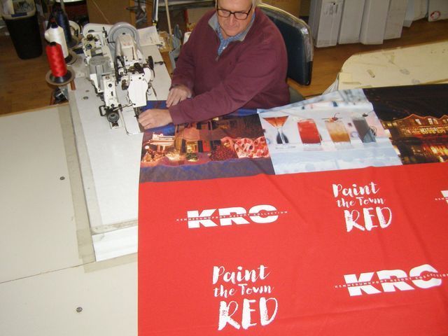A man is sitting at a table making a blanket that says paint the town red