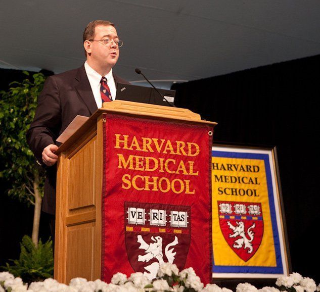 A man stands at a podium with a banner that says Harvard Medical School