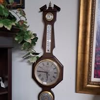Wall clock with brown wood frame, thermometer, barometer, and clock face.