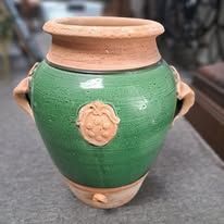 Green ceramic pot with handles, terracotta rim, and fruit embellishment.