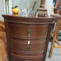 Dark wood cabinet with three drawers; a glass bowl and a decorative lamp on top.