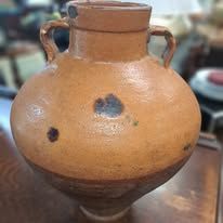 Large, rounded, brown ceramic jar with two handles. The jar has a textured surface with dark spots.