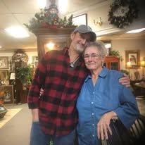 Man and woman smiling in room. Man wears red plaid shirt, woman blue shirt. Interior setting.