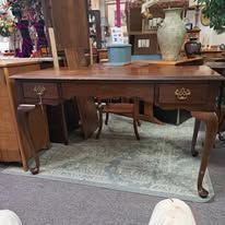 Wooden desk with drawers, set on a light green rug, in a room with antiques and decor.
