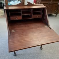 Wooden writing desk with the front panel open, revealing storage compartments.