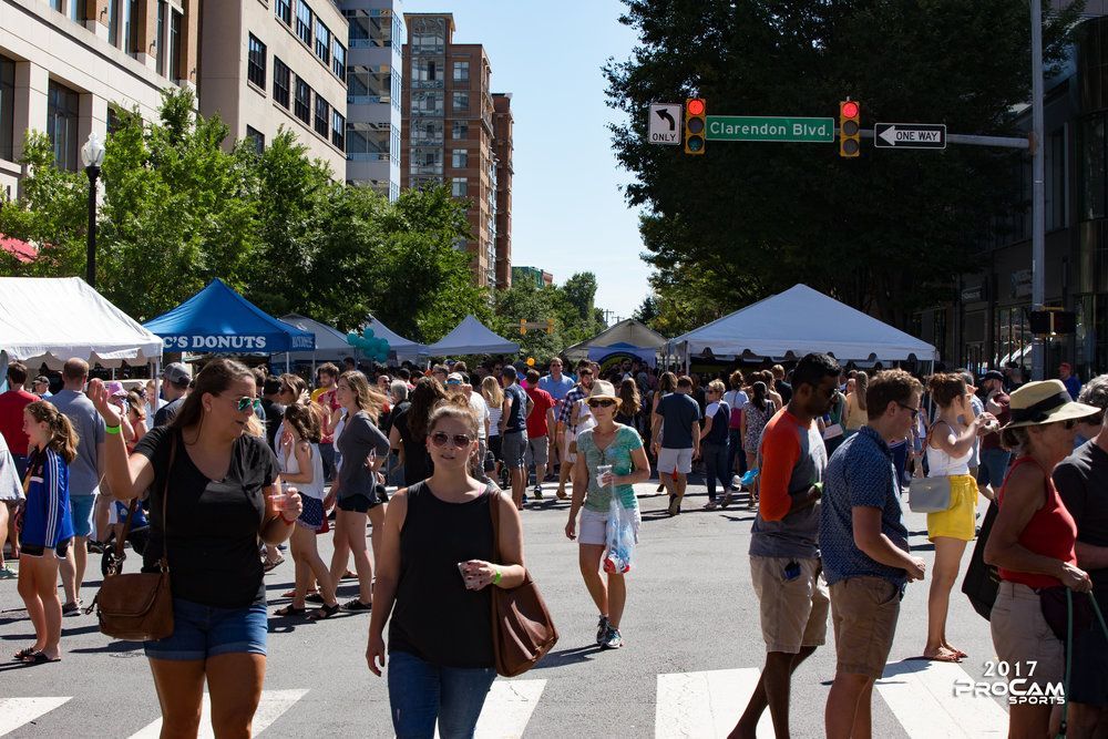 Crowd on Clarendon city street with tents; sunny day, people walking in Virginia