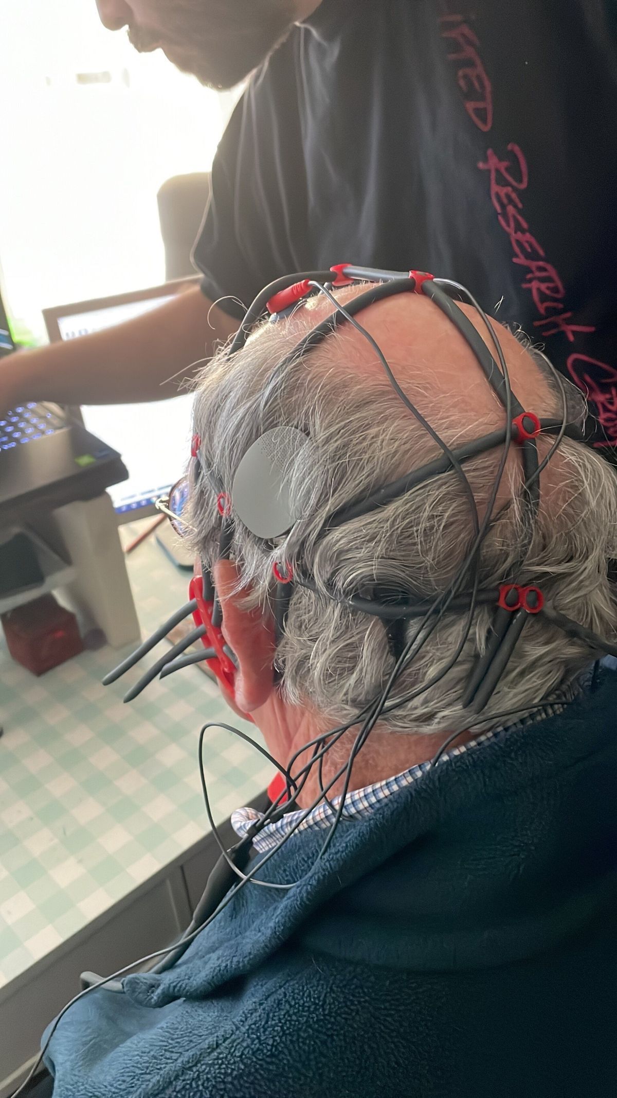 Person wearing an EEG cap for a brain scan. Another person is nearby, possibly operating the machine.