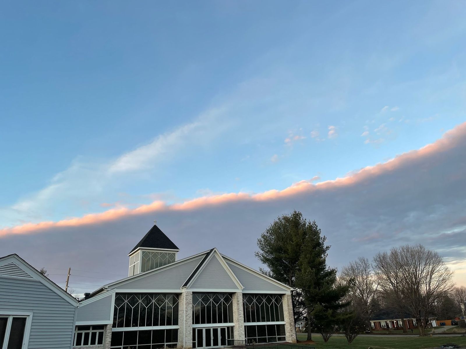A building with a black-roofed tower under a striking pink-tinged cloud formation in a blue sky.