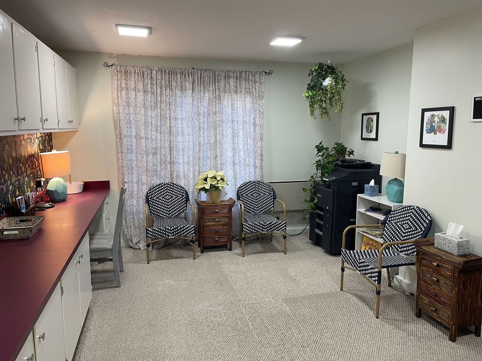 An office waiting area with zebra-patterned chairs, a floral arrangement, and patterned curtains. The room is beige with white cabinets and a burgundy countertop.