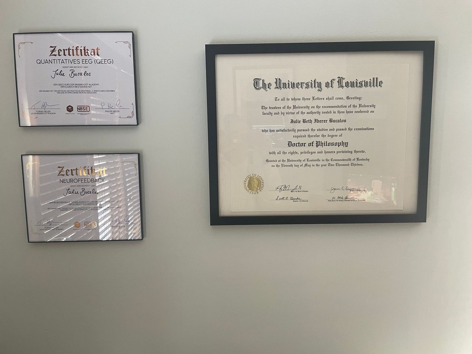 Three framed diplomas on a light gray wall. The largest is from the University of Kentucky.