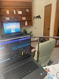 Laptop displaying data, with a monitor and a light stand in a room with shelves, a door, and an armchair.