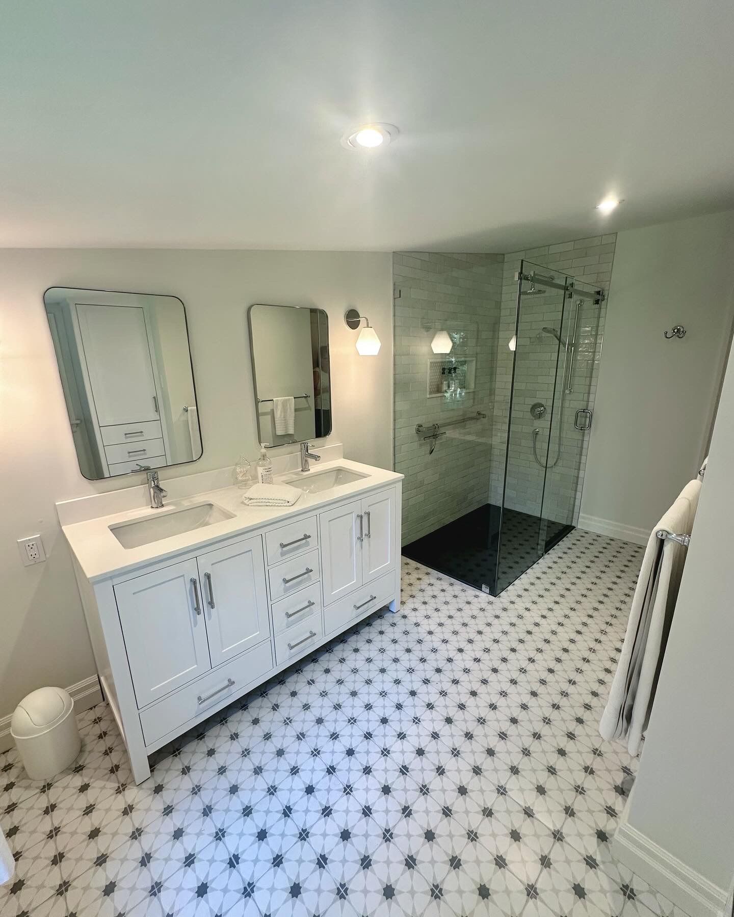 Bathroom with white double vanity, patterned tile floor, and glass shower.