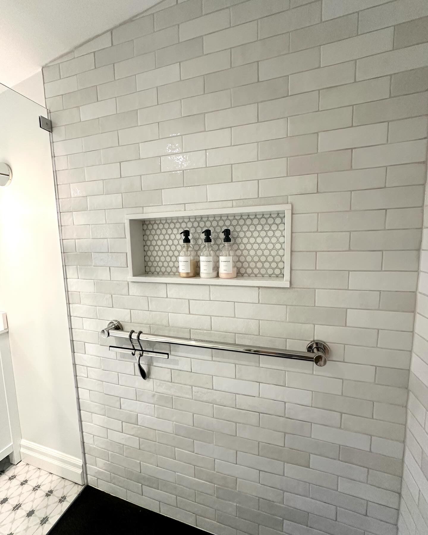 Shower with white subway tile, a recessed shelf with bottles, and a towel bar.