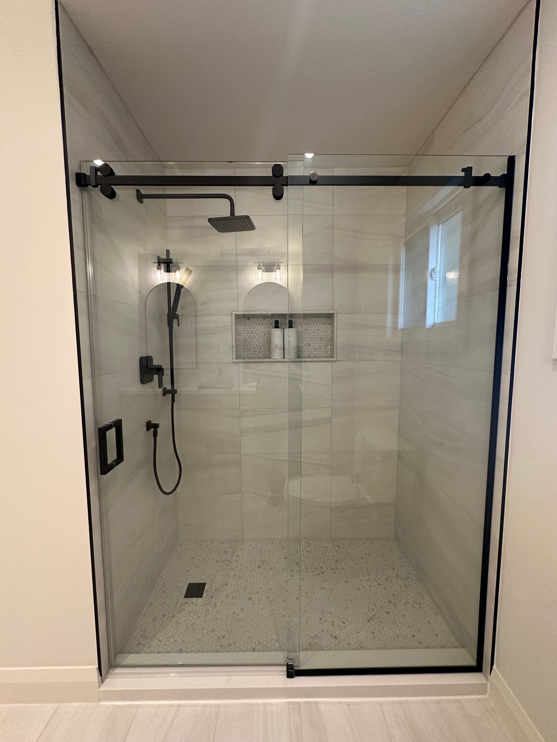 Modern shower with black frame, glass door, and white tile.