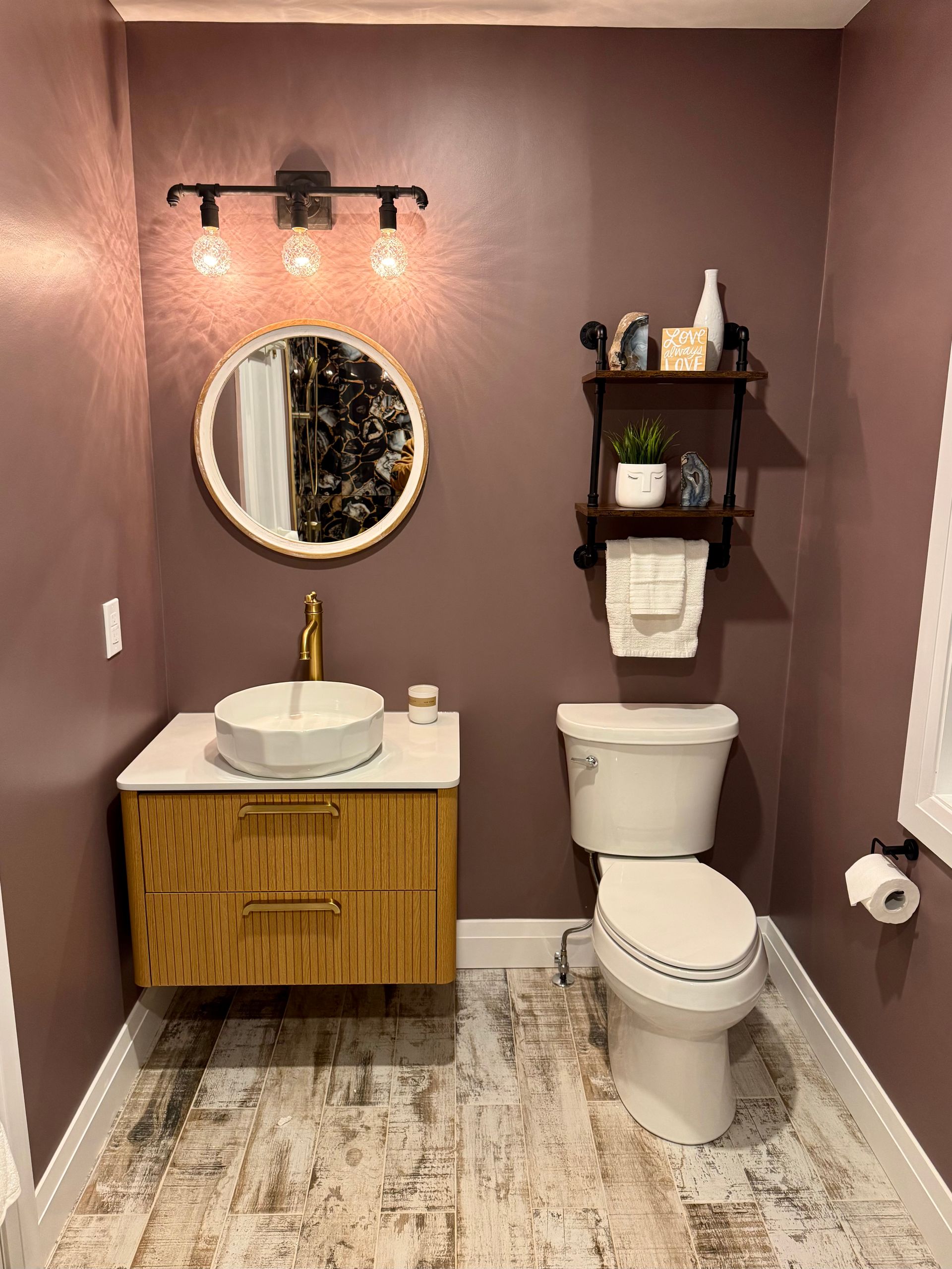 Bathroom with mauve walls, light wood vanity, round mirror, and toilet.