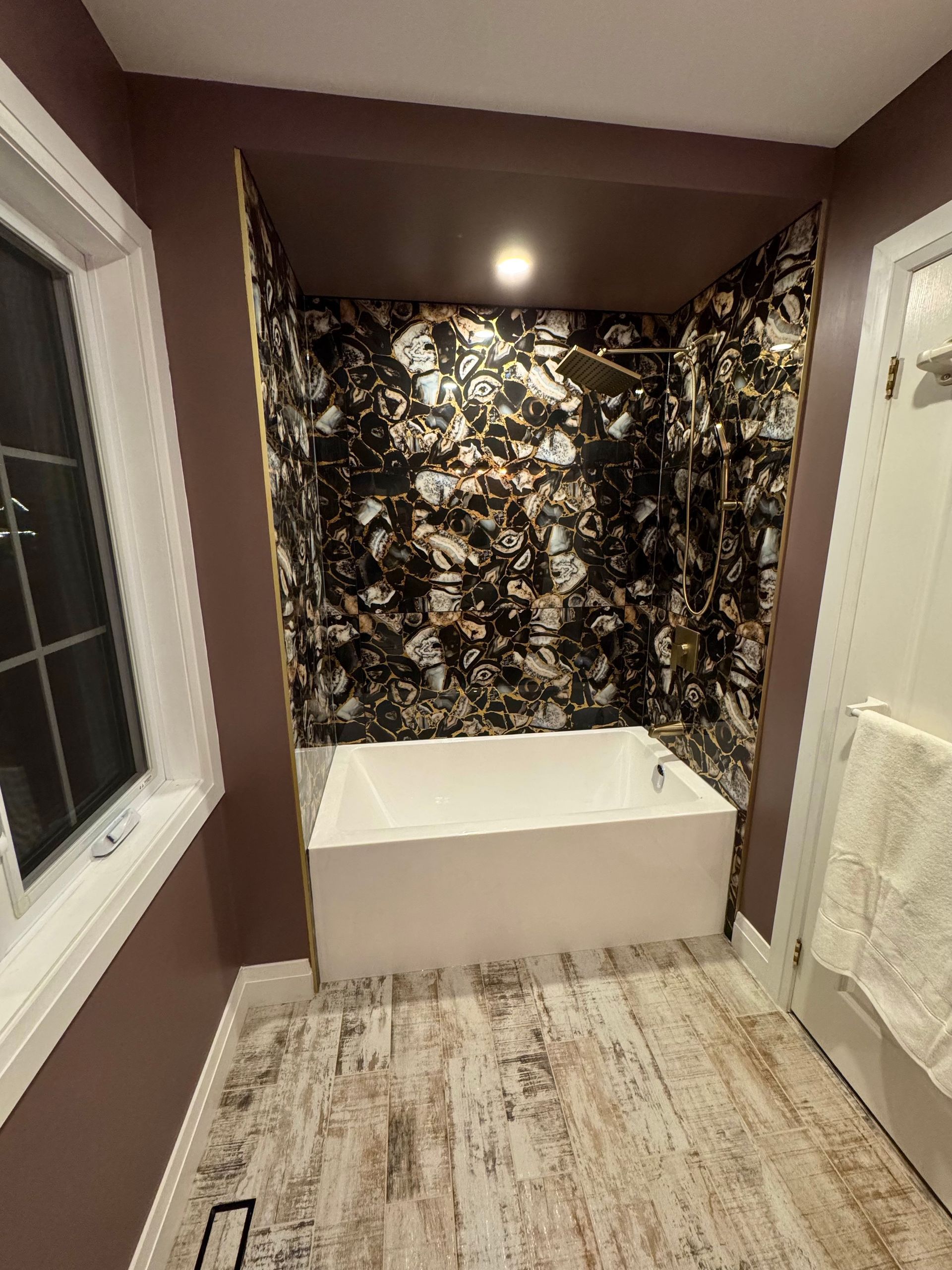 Bathroom with a bathtub beneath a patterned wall. The floor has light wooden planks.