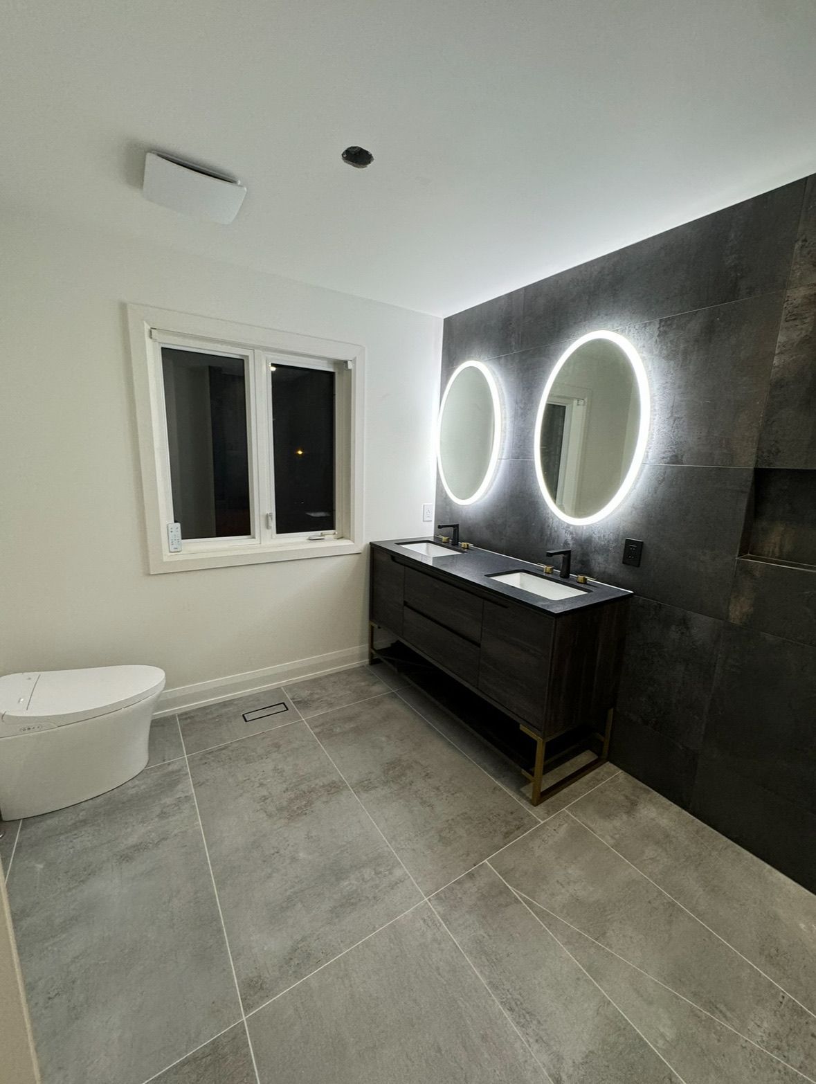 Modern bathroom with a dark vanity, illuminated mirrors, and a freestanding tub.