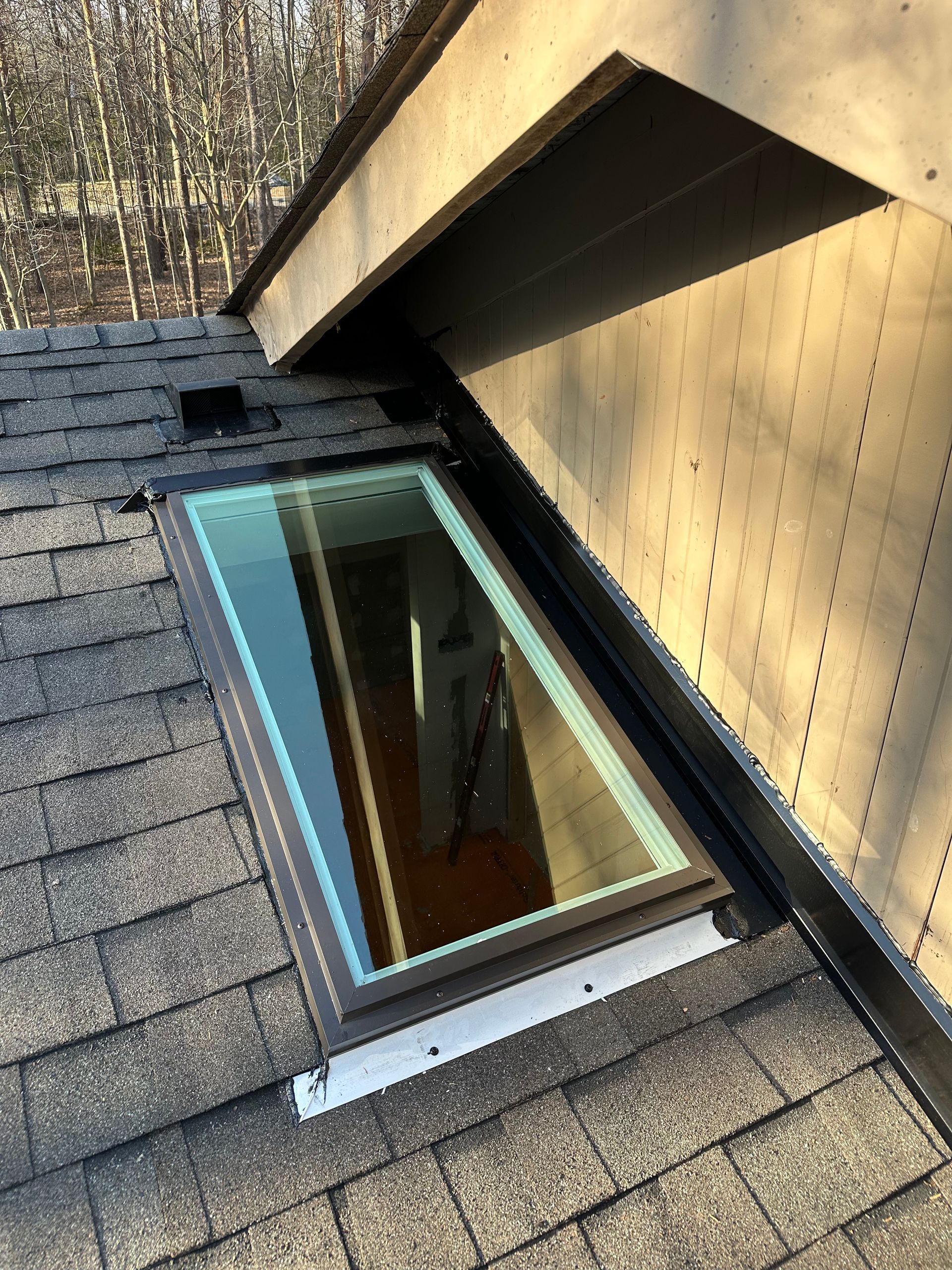 Skylight on a shingled roof, next to a beige wall under an eave.
