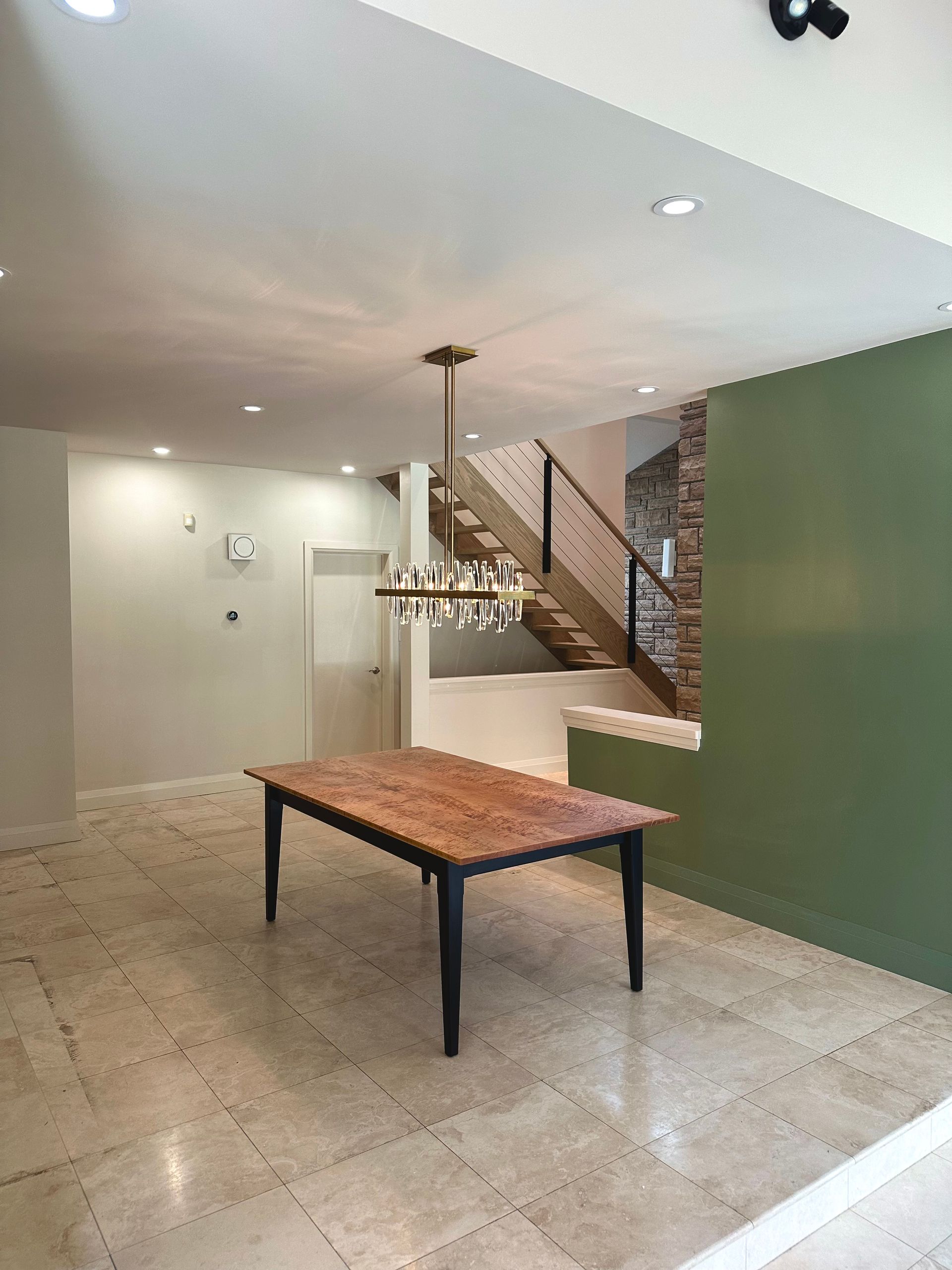 Dining room with wooden table, stairs, green wall, and chandelier.