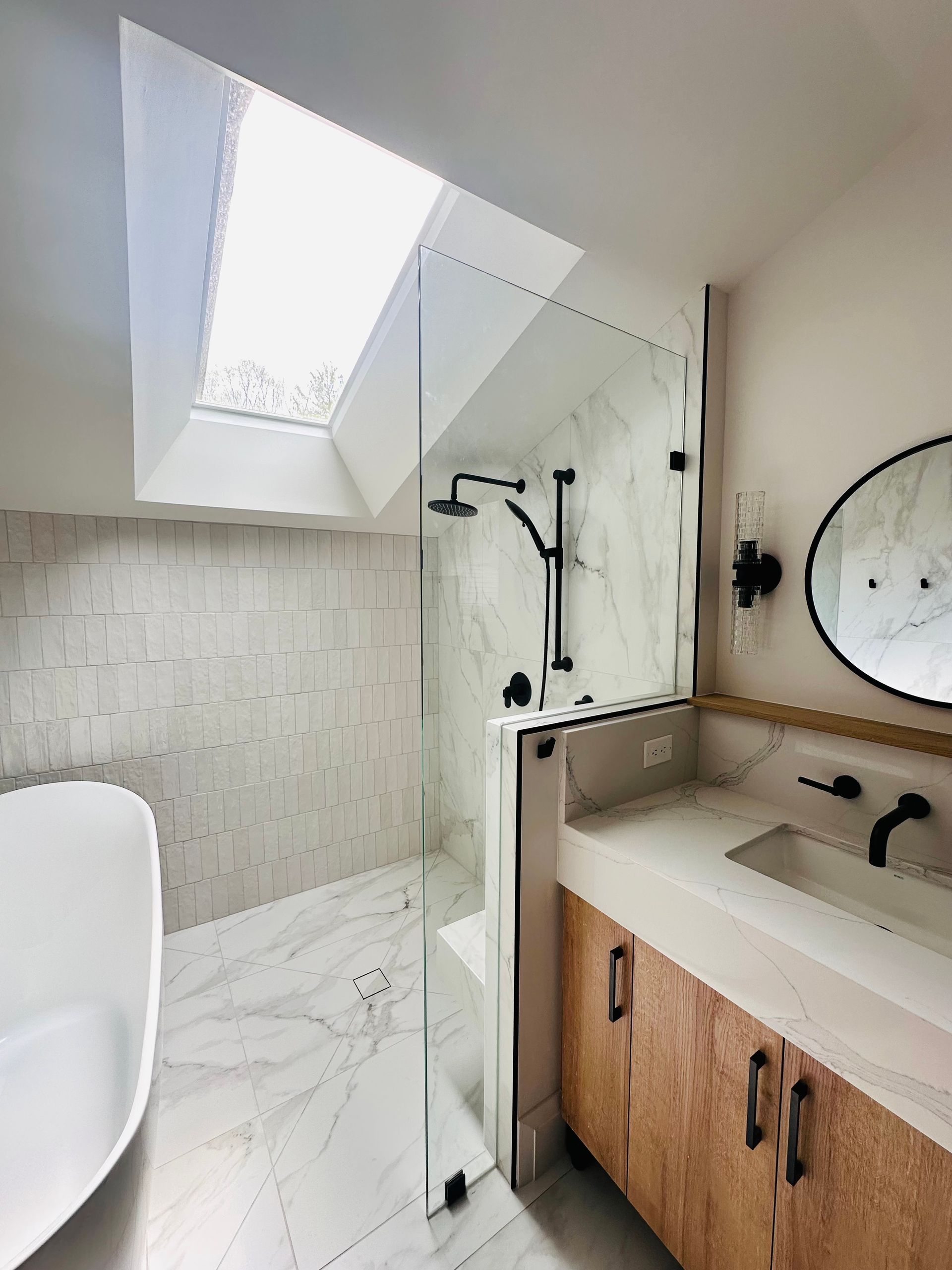 Modern bathroom with a glass-enclosed shower, wood vanity, and a skylight.