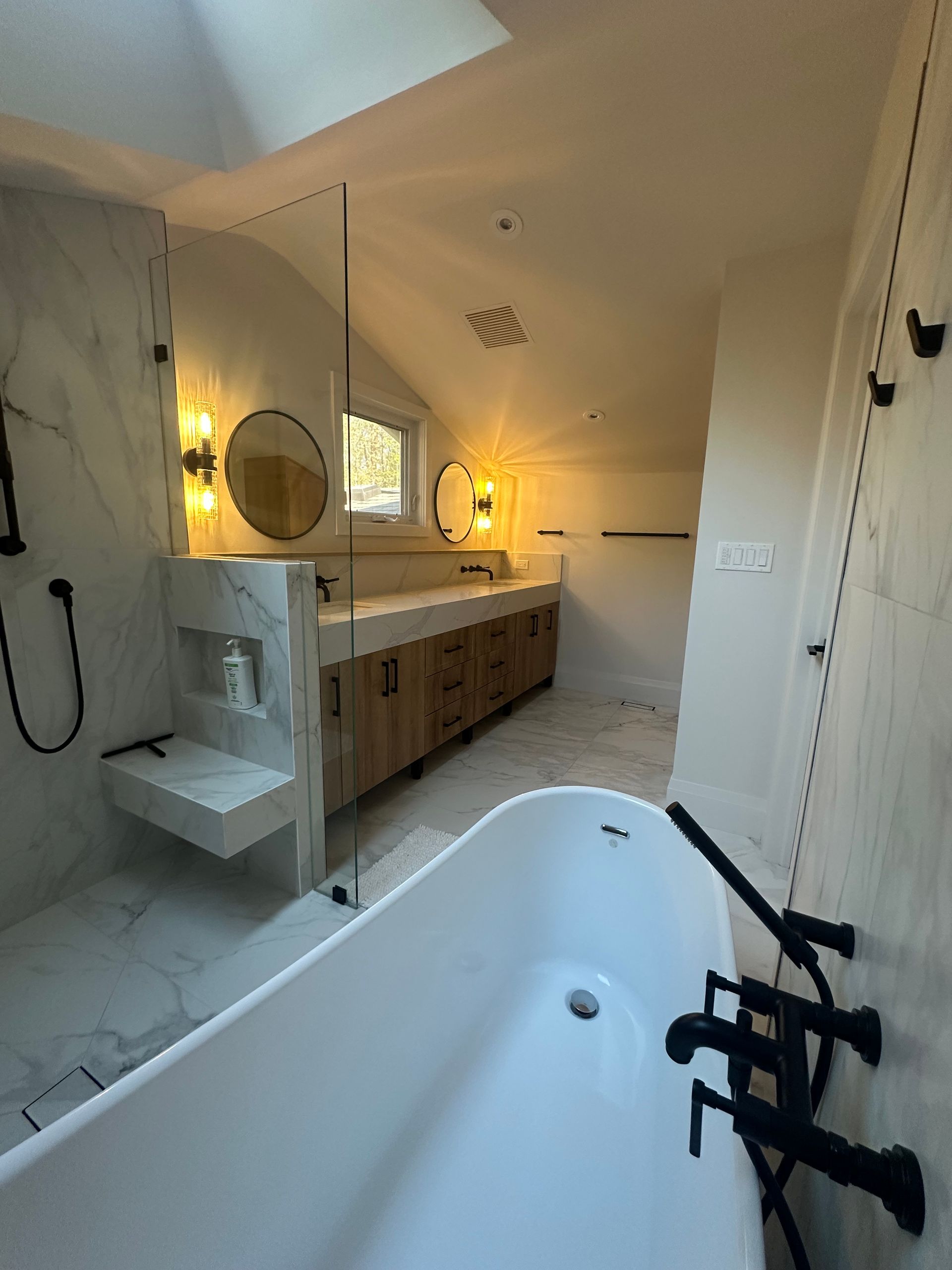 Modern bathroom with white tub, marble walls, wooden cabinets, and black fixtures.