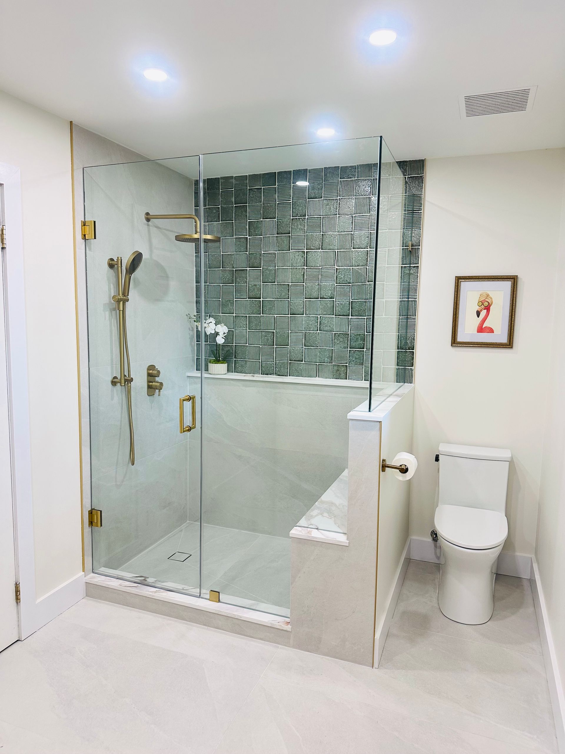 Modern bathroom with glass shower, patterned tile accent wall, and gold fixtures.