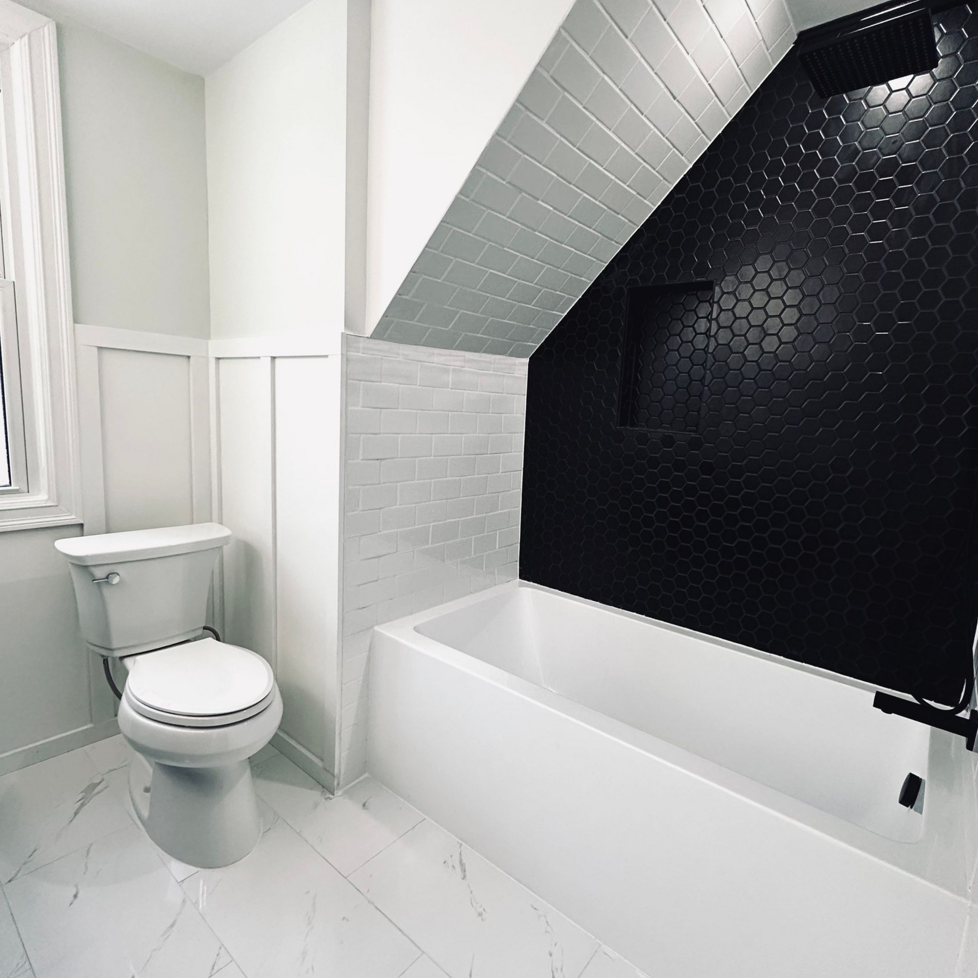 White and black tiled bathroom with a toilet, bathtub, and black hexagon tile accent wall.