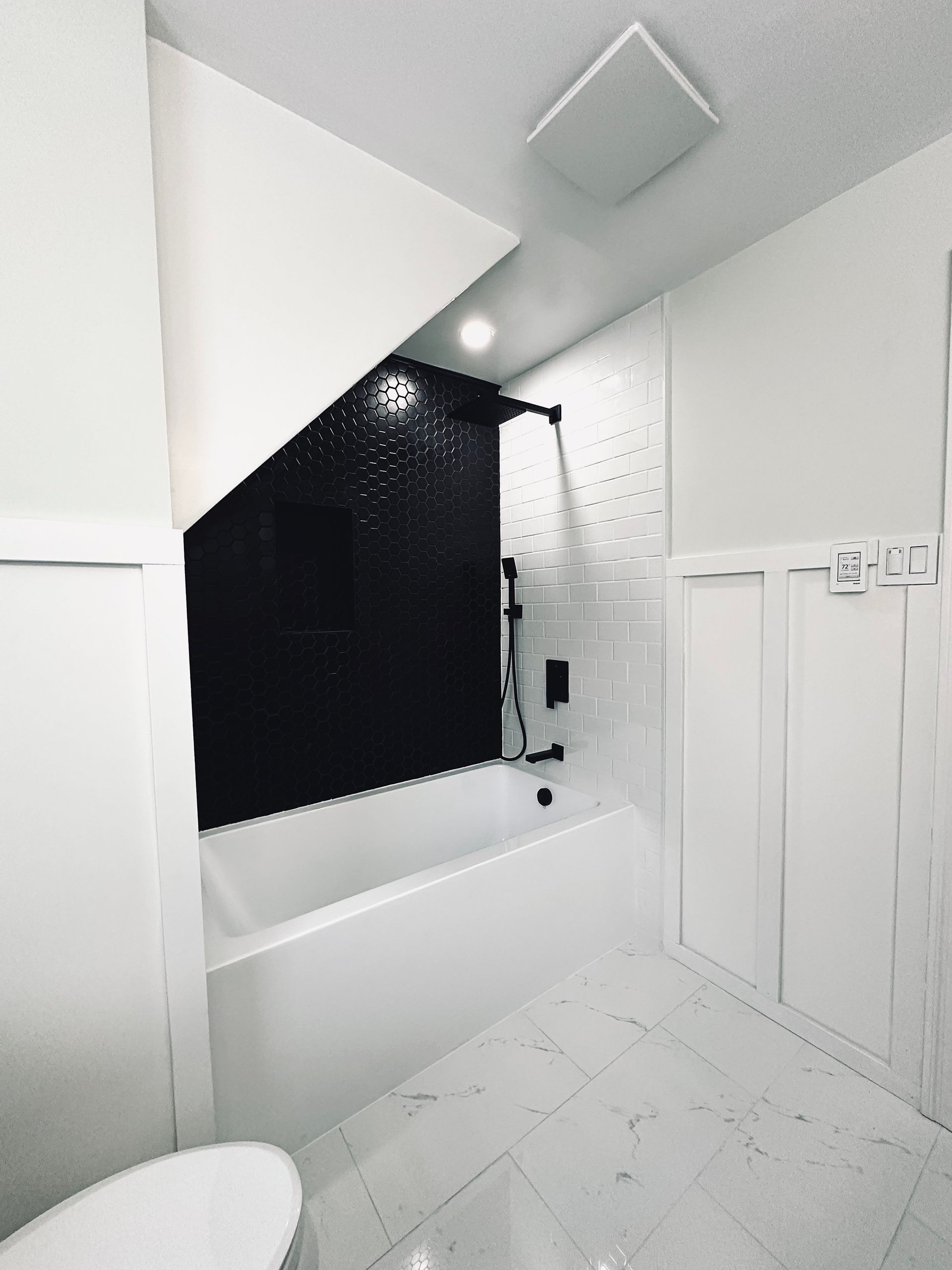 Bathroom with black tiled shower, white tub, and patterned floor.