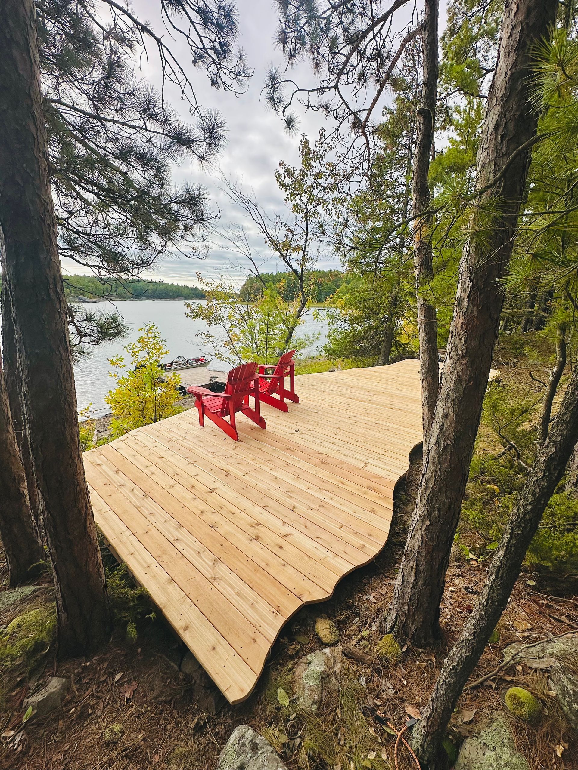 Wooden deck with two red chairs overlooking a lake through trees.
