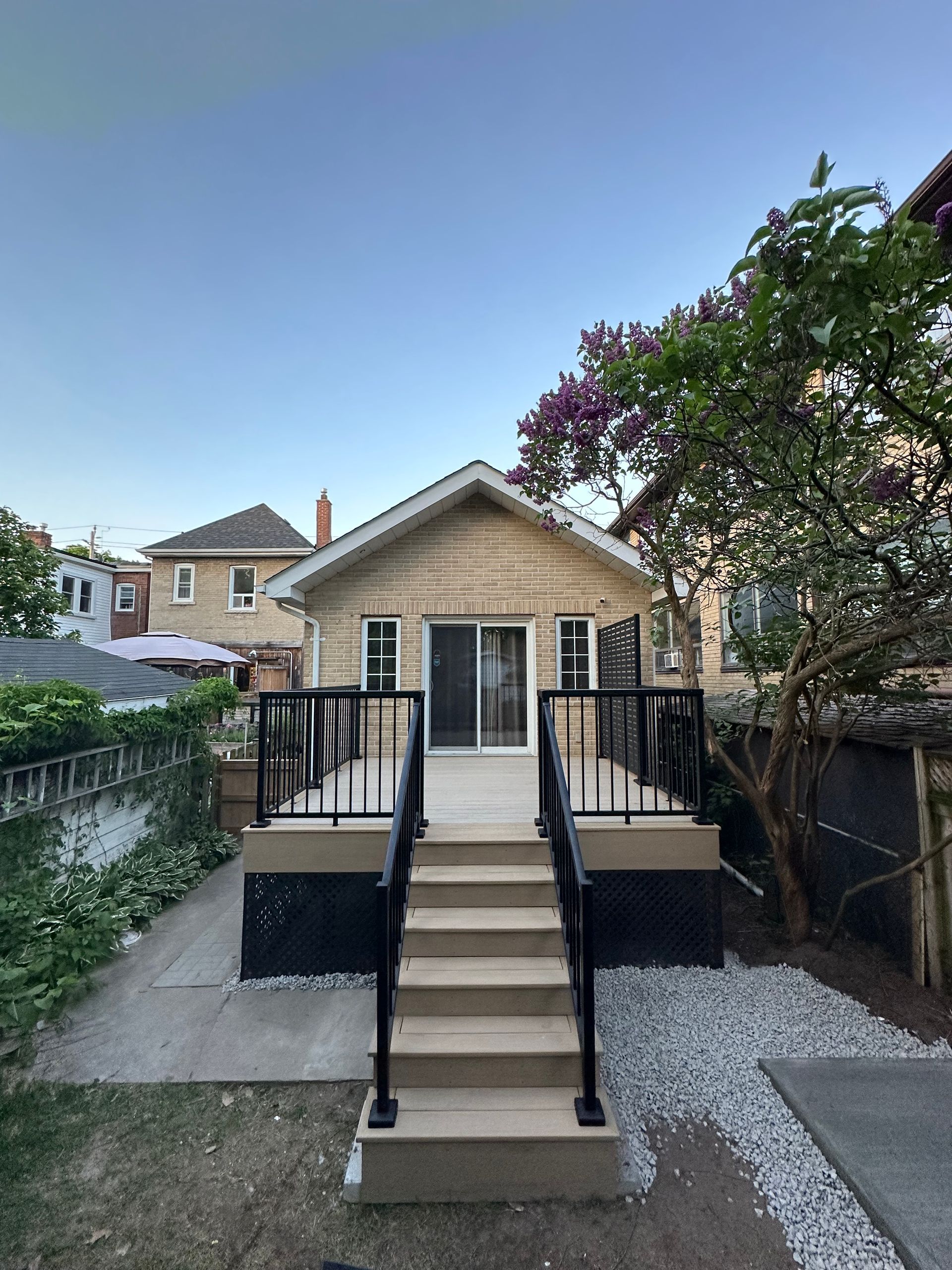 Wooden deck with stairs leading to a house with black railings and light-colored siding.