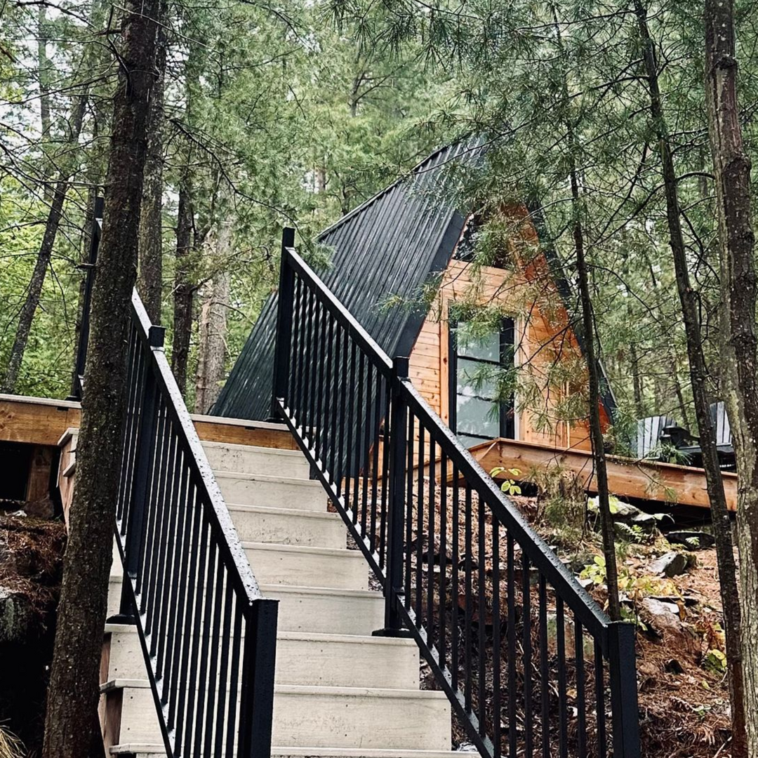 Stairway leading up to a wooden A-frame cabin in a wooded area, surrounded by trees.