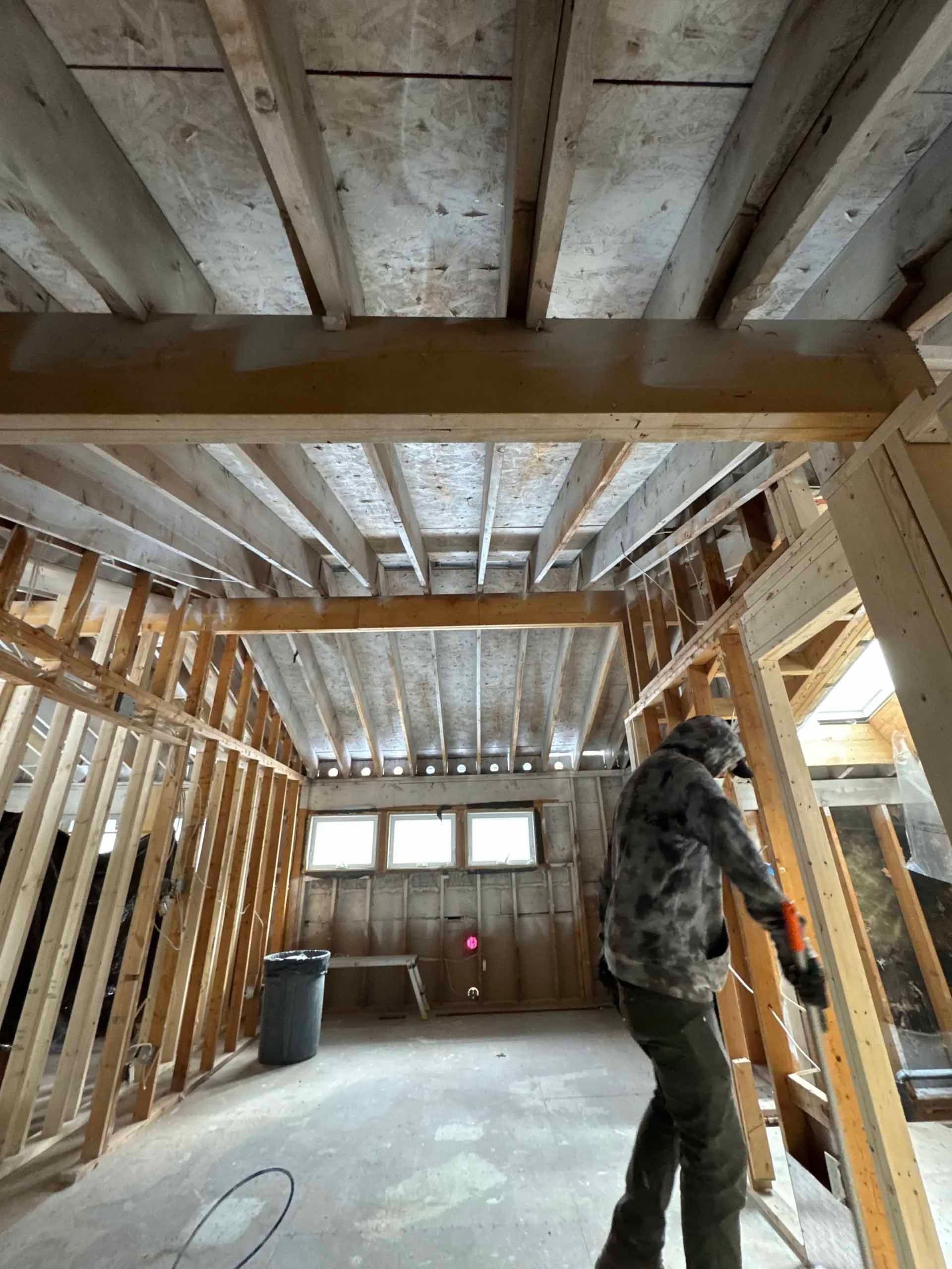 Interior renovation; person holding wood in a room with exposed beams and framing.