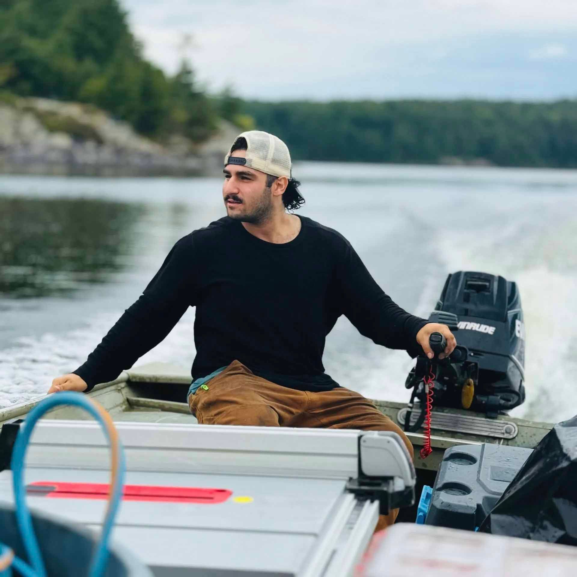 Man in black shirt and cap operating a motorboat on a lake.