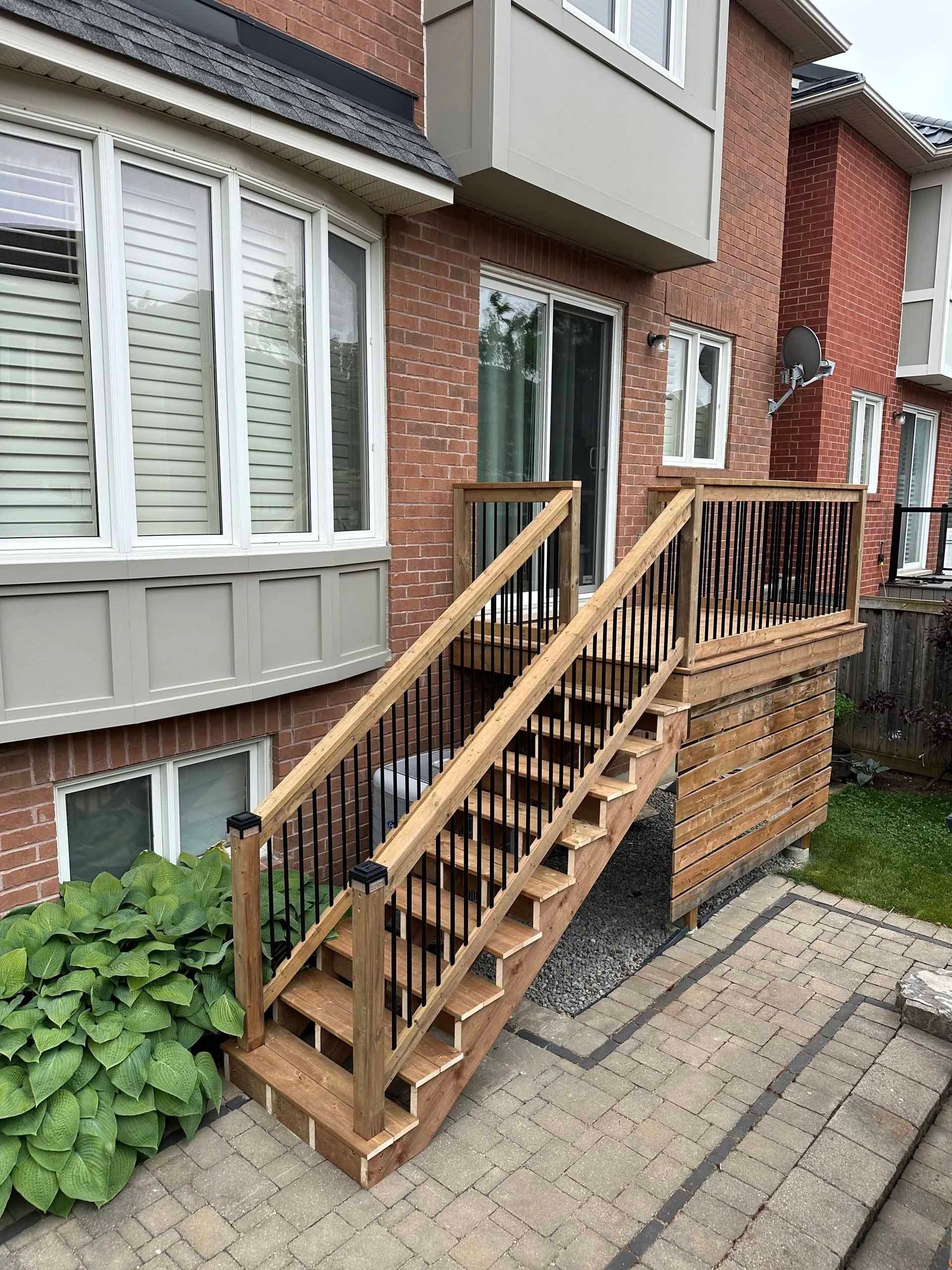 Wooden outdoor staircase with black railings leading up to a deck attached to a brick building.
