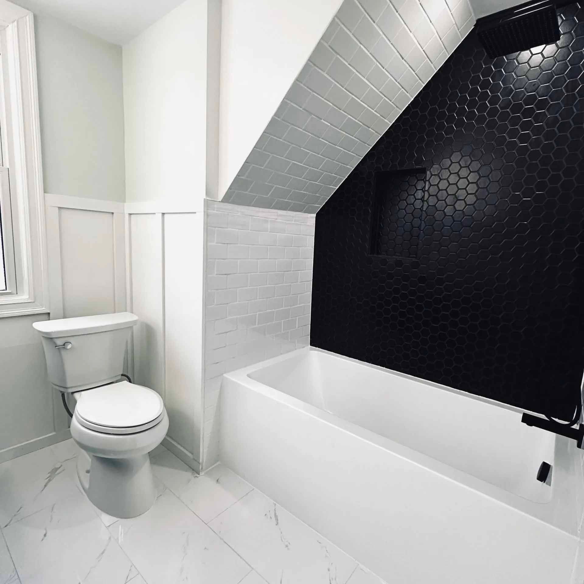 White and black bathroom with bathtub, black tiled shower wall, and marble floor.