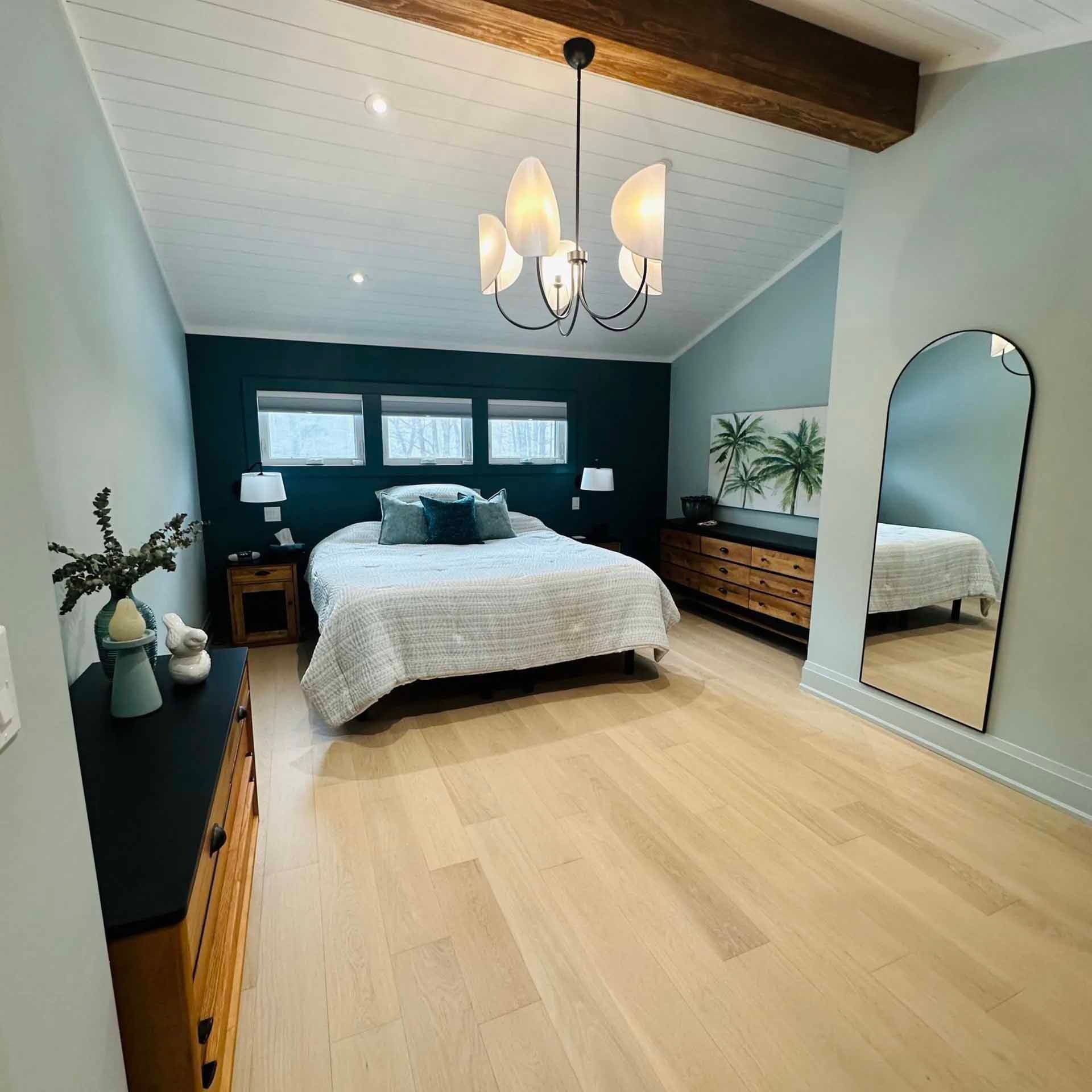Bedroom with blue walls, light wood floor, and a bed. Mirror and dresser are visible.