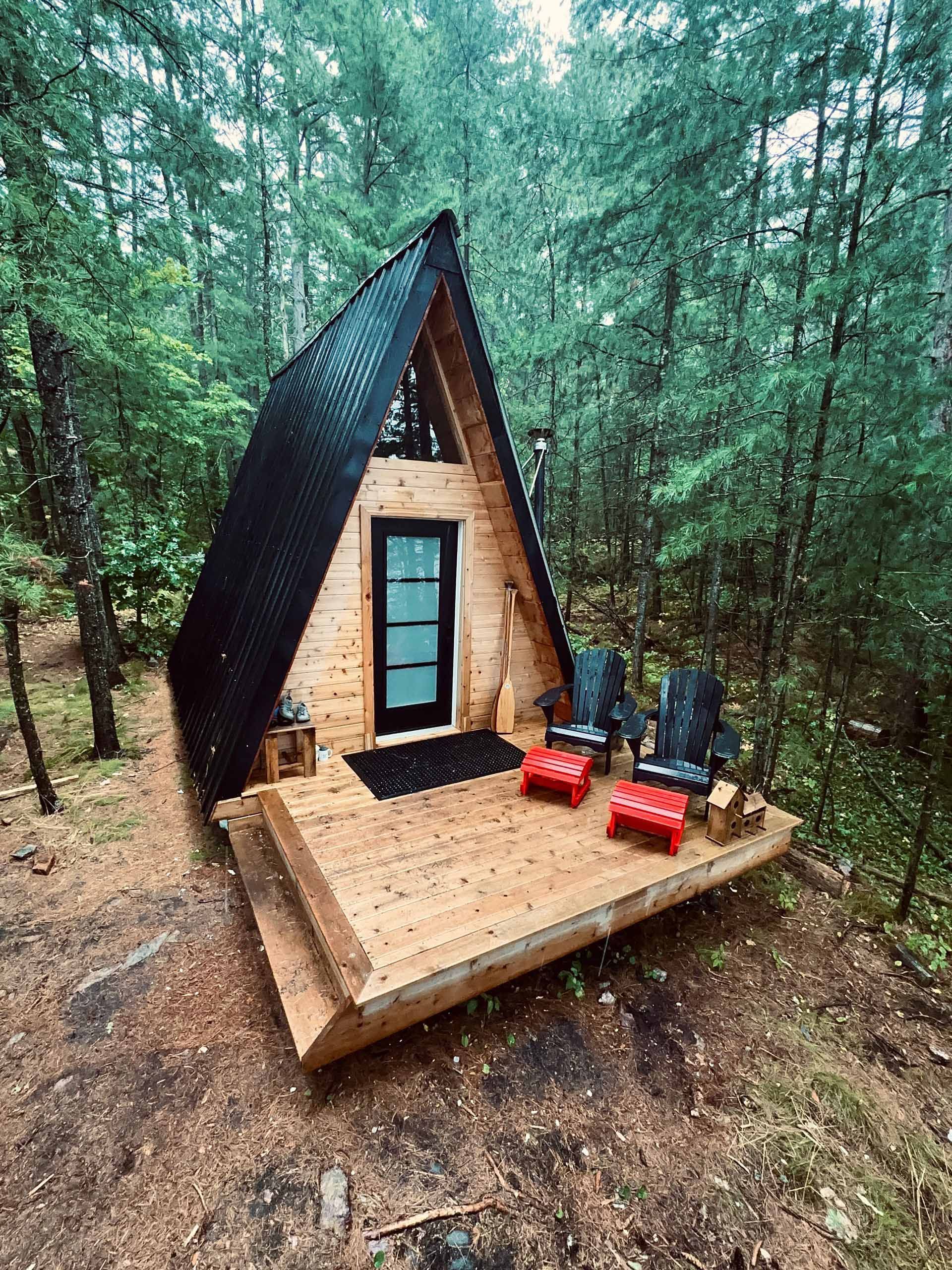 A-frame cabin nestled in a forest, surrounded by trees and a small deck.