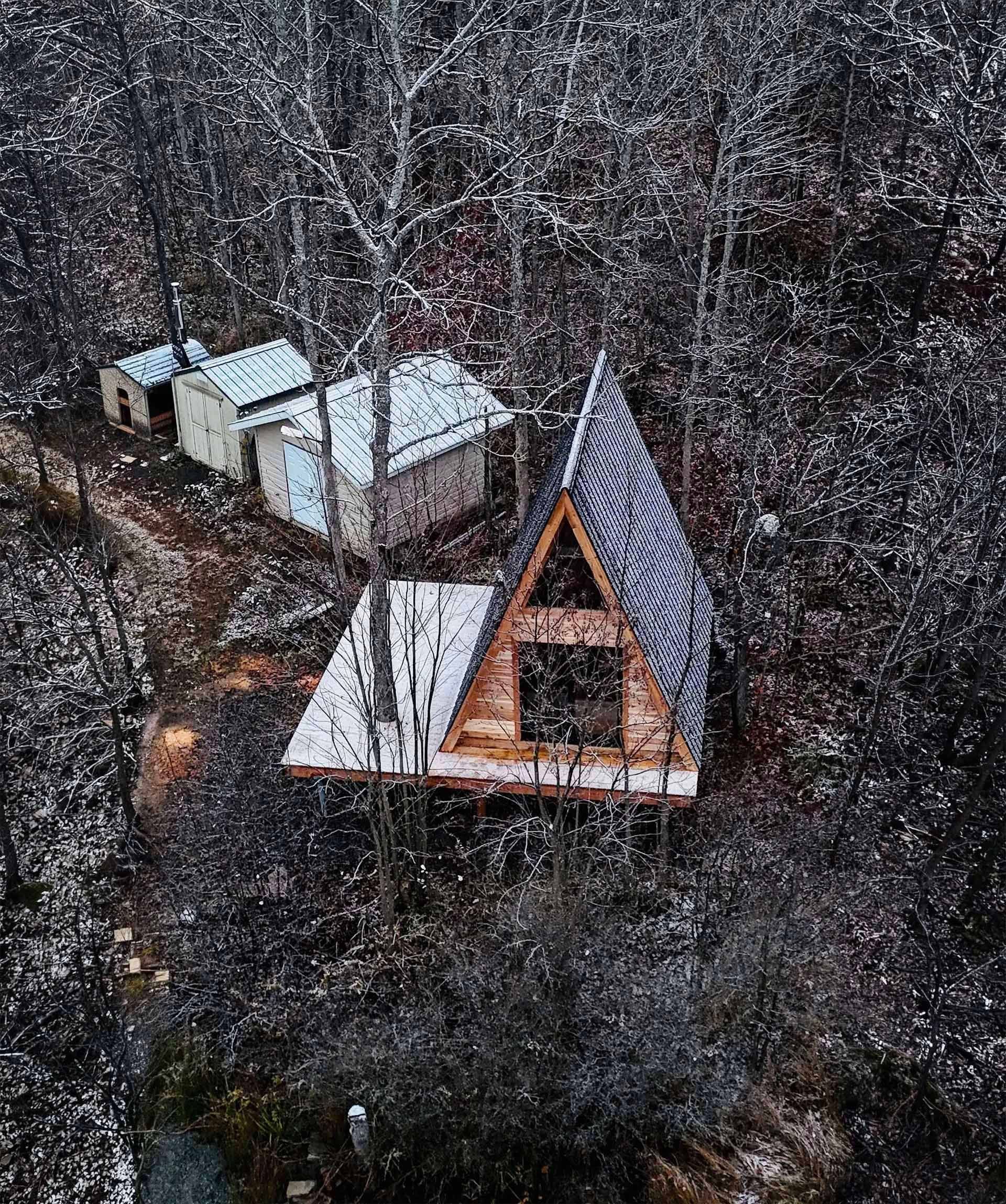 Small brown cabin with porch, two blue chairs, set in a forest.