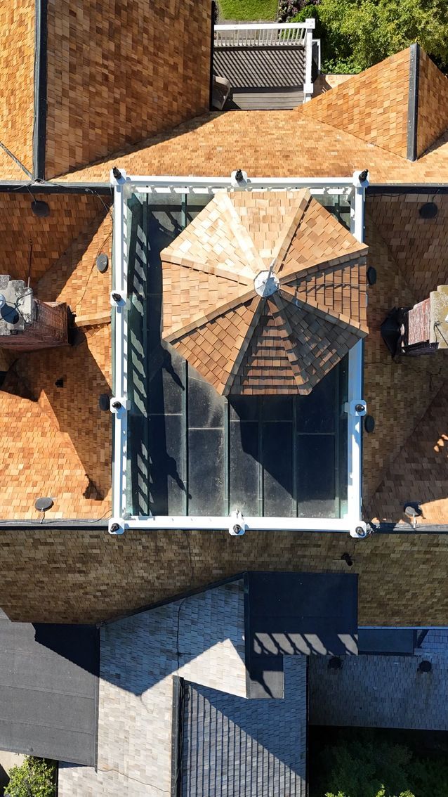 Overhead view of a house roof with a glass-enclosed space and a small, octagonal, brown-shingled structure.