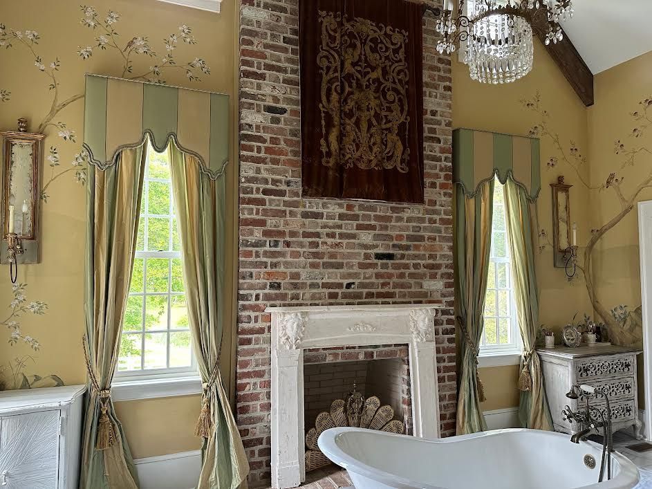 Elegant bathroom with brick fireplace, tub, and window curtains. Yellow walls with floral accents.