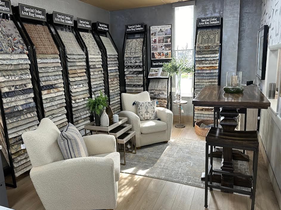 Tile showroom interior: Display racks of tile samples, two armchairs, small table, dark wood counter.