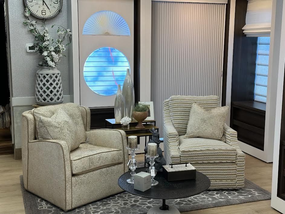 Two patterned armchairs face each other, with a round table in between. Neutral-toned room with decorative accents.