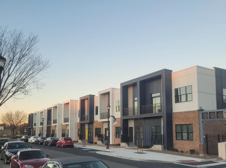 Row of modern townhouses with various colored siding, parked cars on street.
