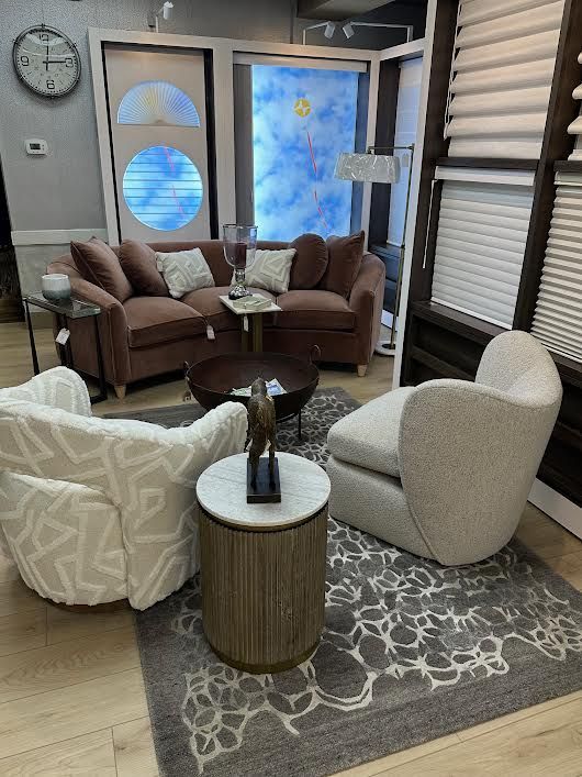 A furniture showroom with a pink sofa, two armchairs, a round coffee table, and area rug.