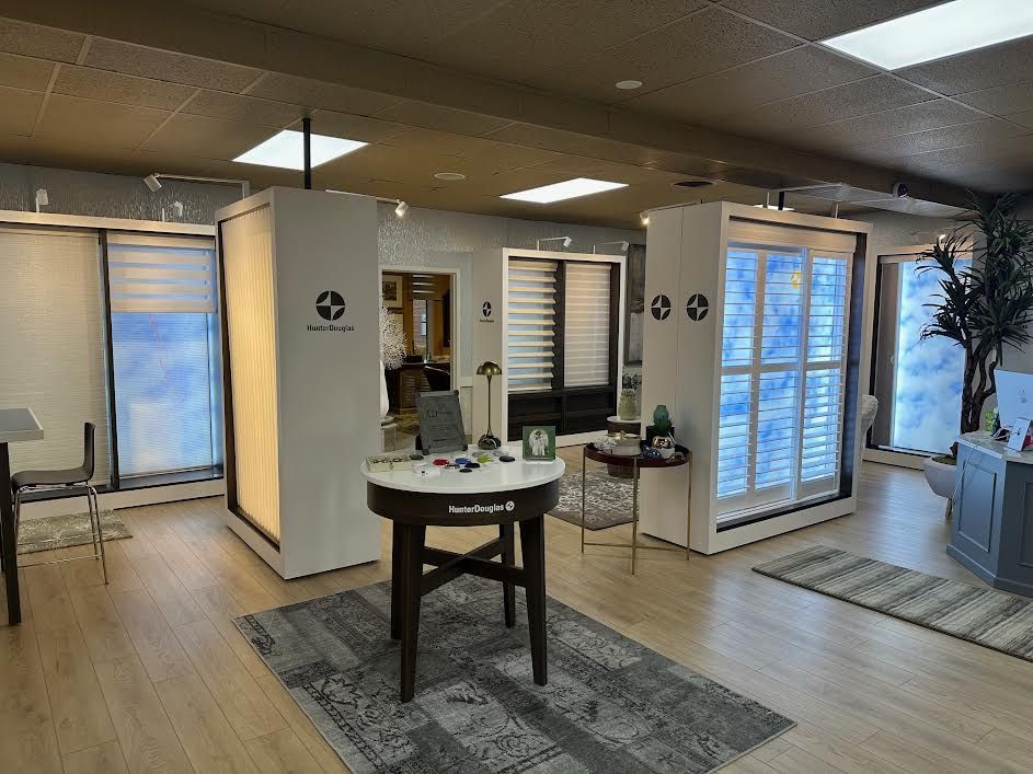 Interior of a showroom with window blinds displays. Includes a central table with samples, and light-colored wood flooring.