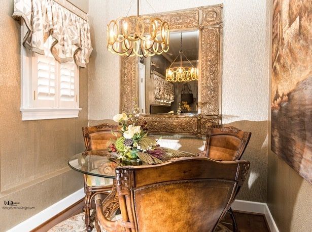 Dining nook with round table, ornate chairs, large mirror, and gold chandelier.