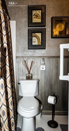 Bathroom with a white toilet, framed art, reed diffuser, and a patterned shower curtain.