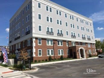 Multi-story apartment building with red brick and grey siding exterior. Parking lot in foreground.