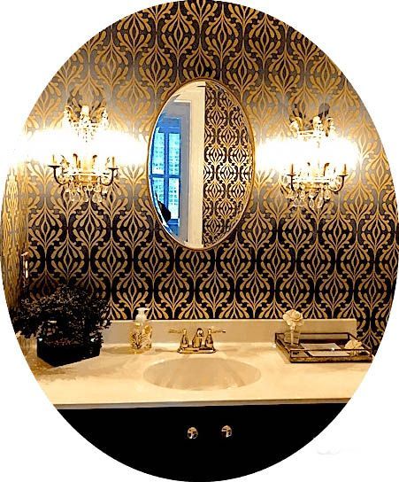 Bathroom vanity with gold patterned wallpaper, oval mirror, sconces, and black cabinet.